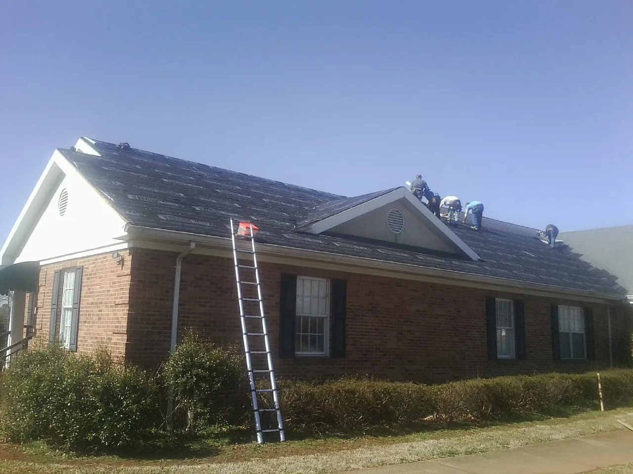 Crew tearing shingles off a brick ranch roof with a ladder set — Metal Roof Repair work by our crew in Pelham