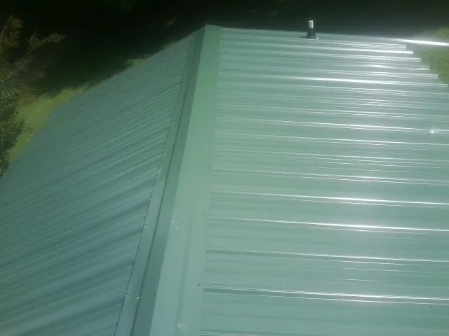 New green metal panels meeting at the ridge of a roof — Flat Roof Repair work by our crew in Pelham