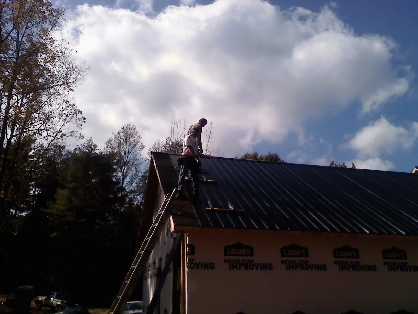 Roofer fastening dark metal panels high against a cloudy sky, from a Roof Inspection job in Pelham